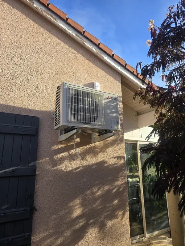 Groupe extérieur de climatisation Mitsubishi Electric fixé en façade, à côté d'une baie vitrée