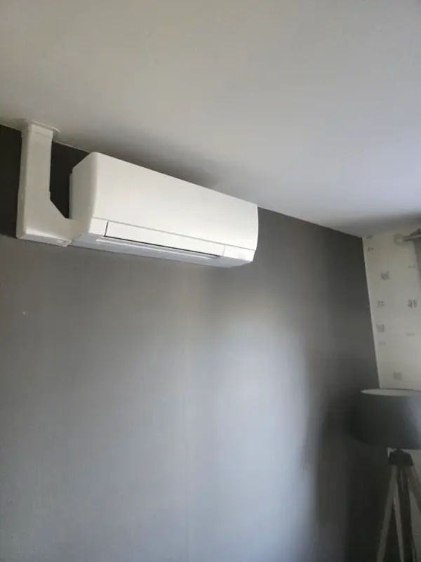 Climatiseur mural avec goulotte blanche coudée sur un mur gris