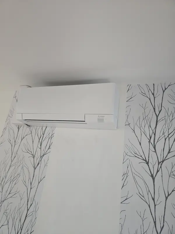 Climatiseur mural installé entre deux lés de papier peint à motifs d'arbres