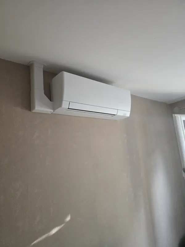 Climatiseur mural avec goulotte descendant du plafond, mur beige